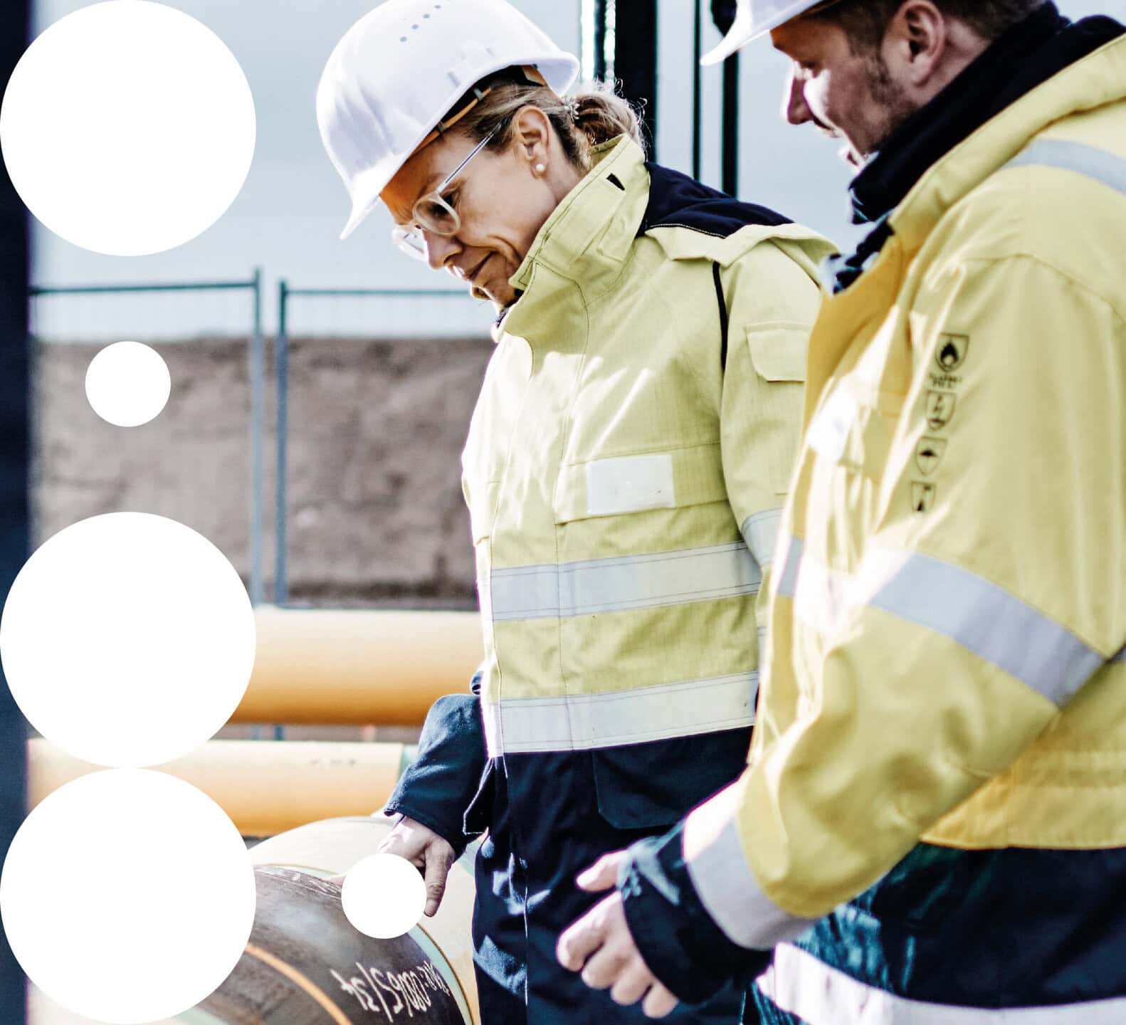 Ontras Zitronengrau: Zwei Mitarbeitende mit Schutzhelmen und Warnkleidung prüfen Rohrleitungen auf einer Industrieanlage.