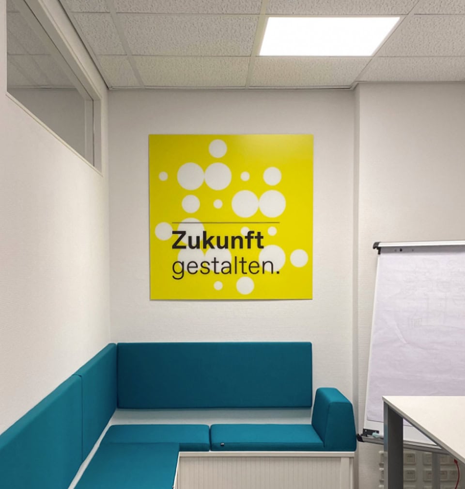 Besprechungsbereich mit Wandbild und dem Leitsatz ‚Zukunft gestalten.‘ im Corporate Design.